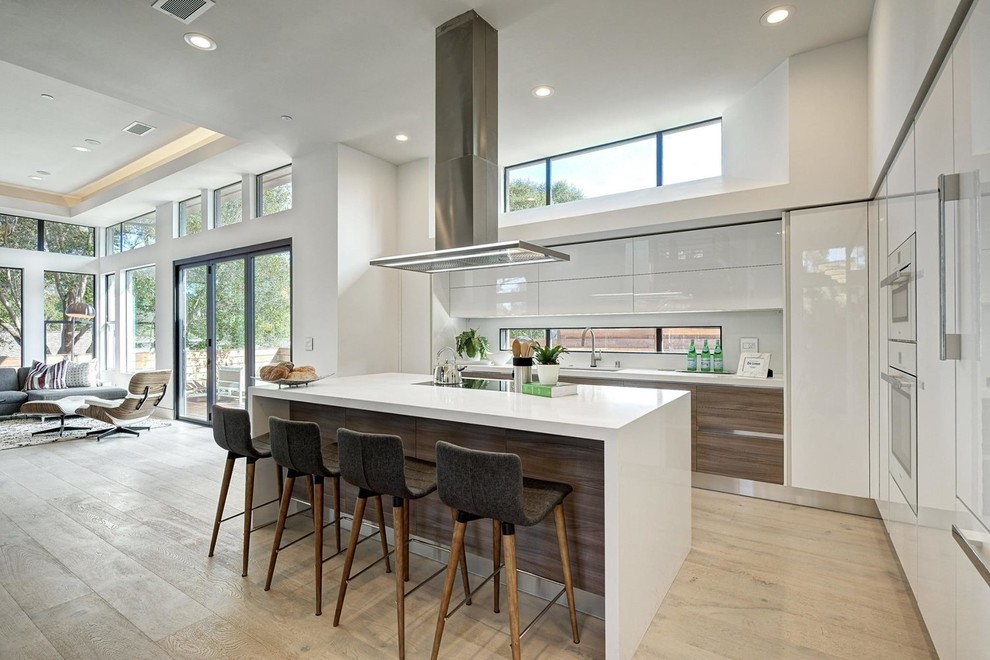 This is an example of a contemporary open plan kitchen in San Francisco with an undermount sink, flat-panel cabinets, white cabinets, white appliances, light hardwood floors, with island and white benchtop.