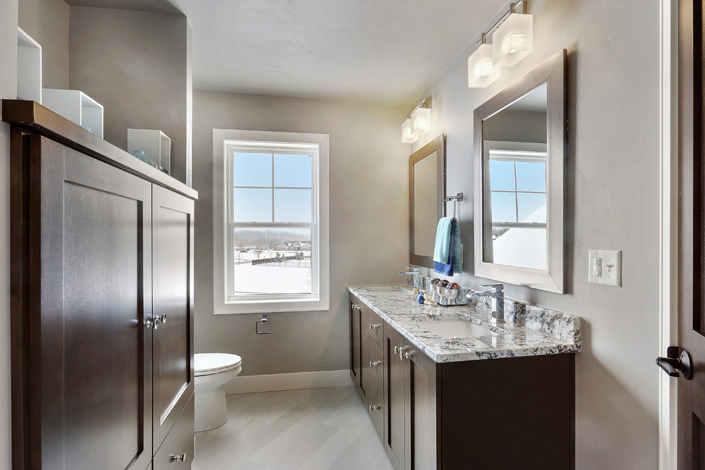 Example of a transitional alcove bathtub design with shaker cabinets, medium tone wood cabinets, a two-piece toilet, an undermount sink, granite countertops and gray walls