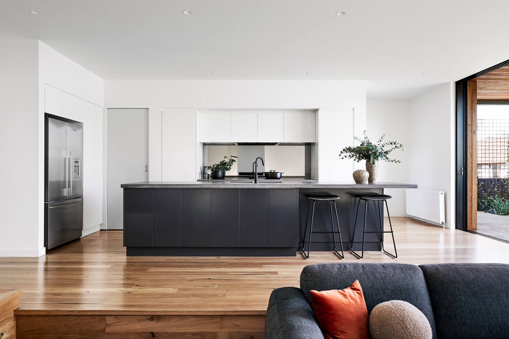 Inspiration for a medium sized contemporary l-shaped kitchen pantry in Melbourne with white cabinets, concrete worktops, mirror splashback, light hardwood flooring and an island.