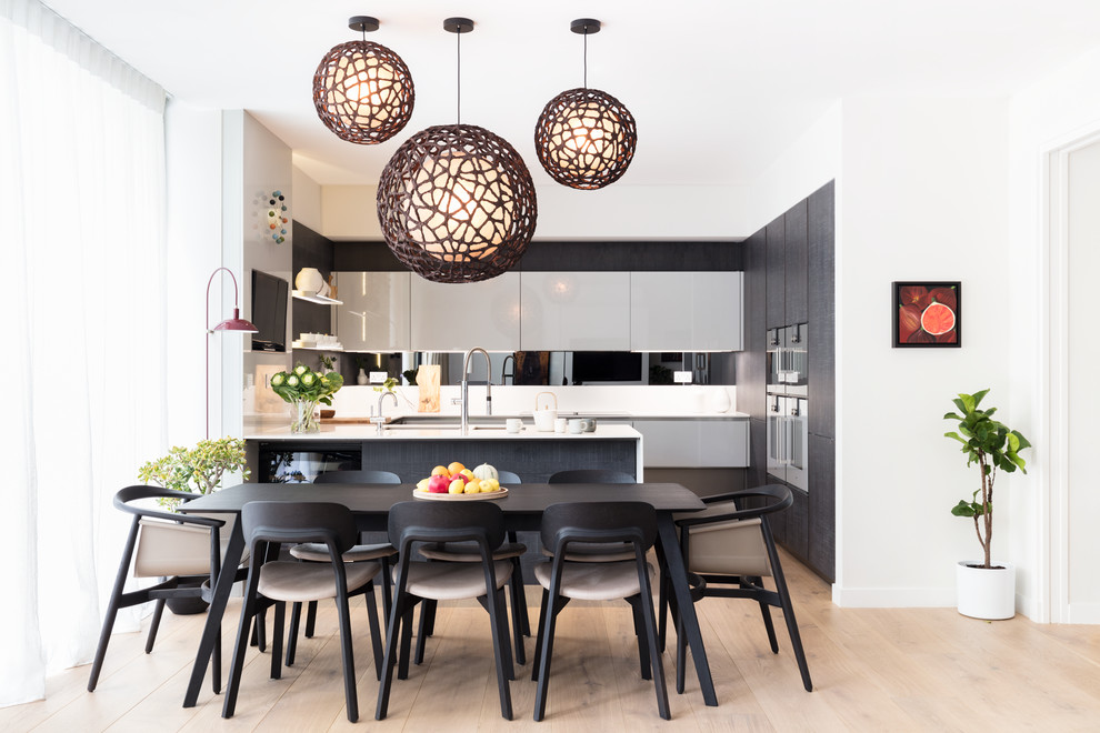 This is an example of a large contemporary kitchen/dining combo in London with white walls and light hardwood floors.