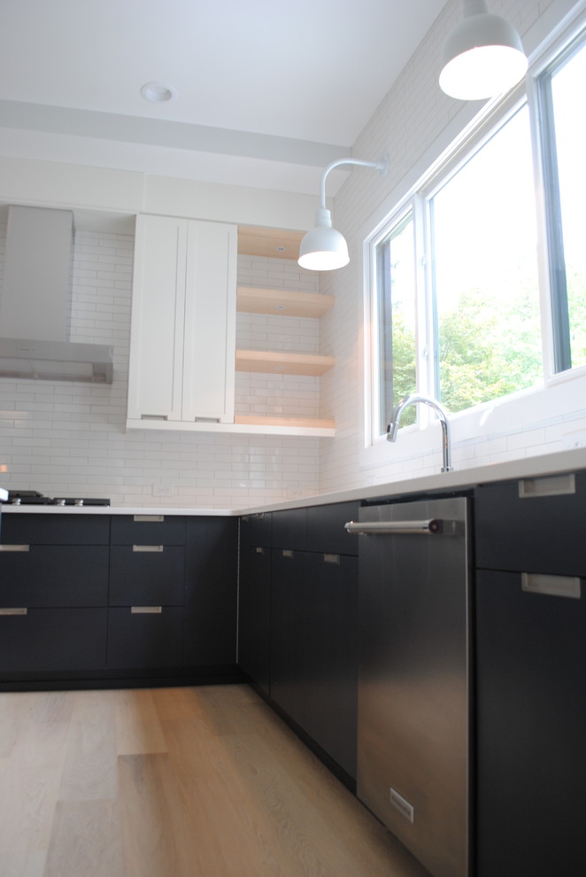 Inspiration for a mid-sized scandinavian u-shaped open plan kitchen in Raleigh with an undermount sink, flat-panel cabinets, black cabinets, quartz benchtops, white splashback, subway tile splashback, stainless steel appliances and light hardwood floors.