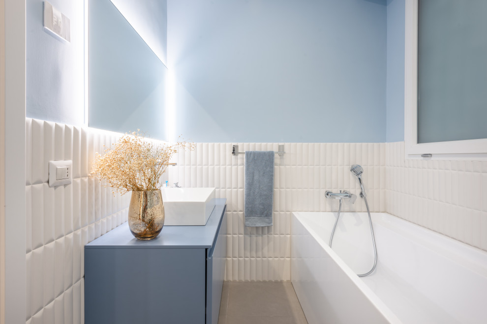 На фото: ванная комната среднего размера в современном стиле с бирюзовыми фасадами, угловой ванной, белой плиткой, синими стенами, настольной раковиной и тумбой под одну раковину с