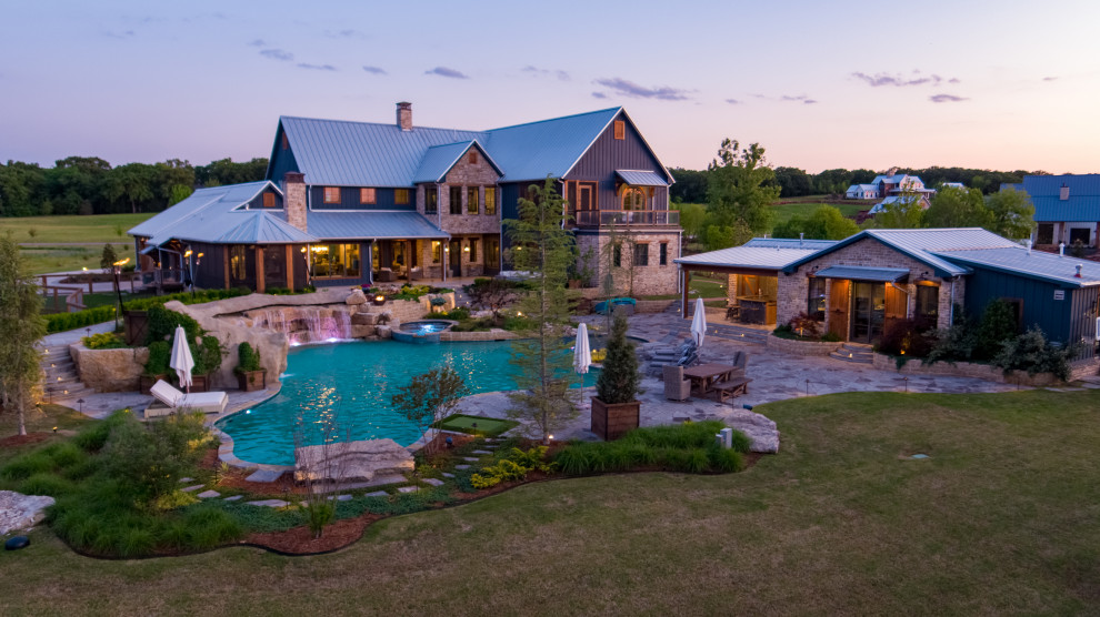 Photo of an expansive country backyard custom-shaped natural pool in Oklahoma City with a pool house and natural stone pavers.