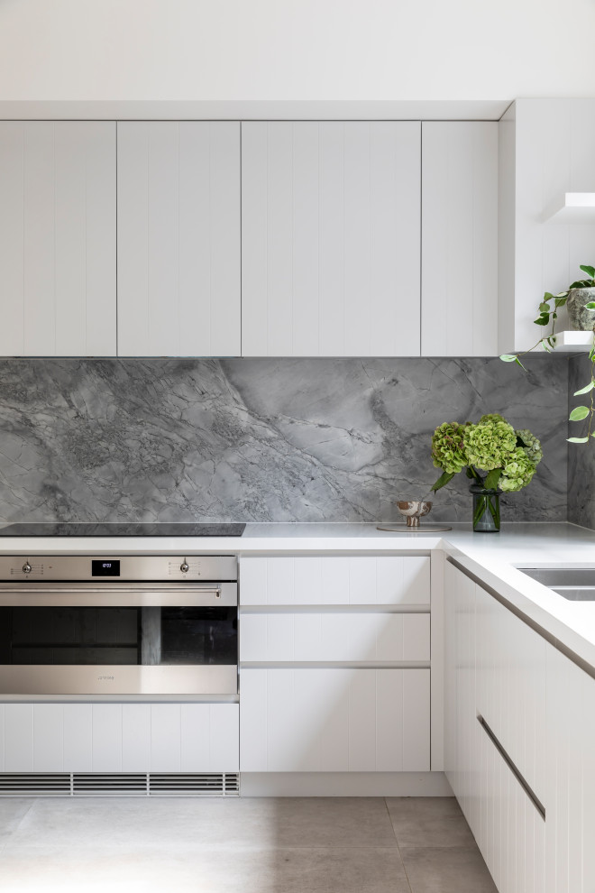 Mid-sized modern l-shaped open plan kitchen in Sydney with an undermount sink, white cabinets, marble benchtops, grey splashback, marble splashback, stainless steel appliances, ceramic floors, with island, beige floor and grey benchtop.