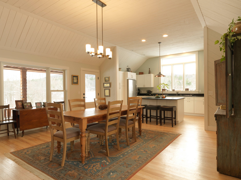 Design ideas for a mid-sized country l-shaped eat-in kitchen in Burlington with white cabinets, granite benchtops, stainless steel appliances, light hardwood floors, with island, brown floor, black benchtop and timber.