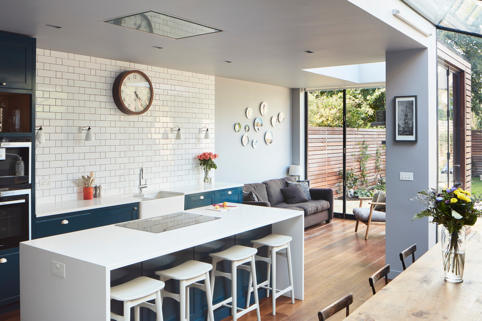 Inspiration for a large contemporary single-wall open plan kitchen in London with a farmhouse sink, blue cabinets, quartzite benchtops, white splashback, dark hardwood floors, with island, shaker cabinets, cement tile splashback, panelled appliances, white benchtop and vaulted.