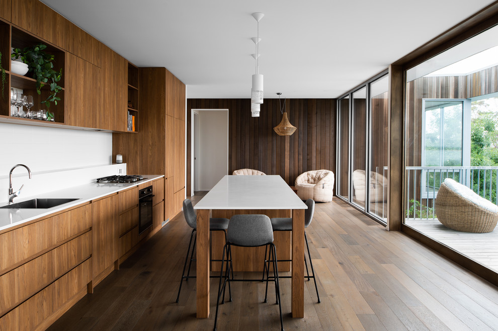 Design ideas for a mid-sized contemporary galley eat-in kitchen in Hobart with an undermount sink, flat-panel cabinets, medium wood cabinets, white splashback, panelled appliances, medium hardwood floors, with island, brown floor, white benchtop, laminate benchtops and limestone splashback.