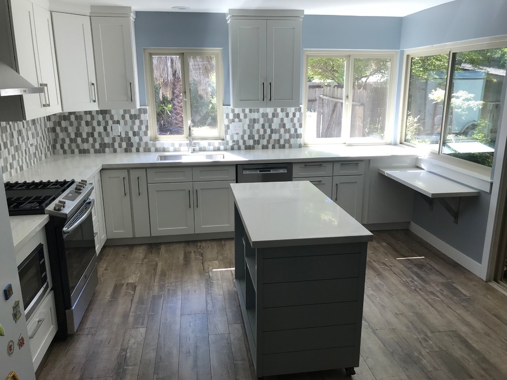 Inspiration for a mid-sized transitional l-shaped laminate floor and brown floor eat-in kitchen remodel with an undermount sink, shaker cabinets, white cabinets, quartzite countertops, multicolored backsplash, glass sheet backsplash, stainless steel appliances, an island and white countertops