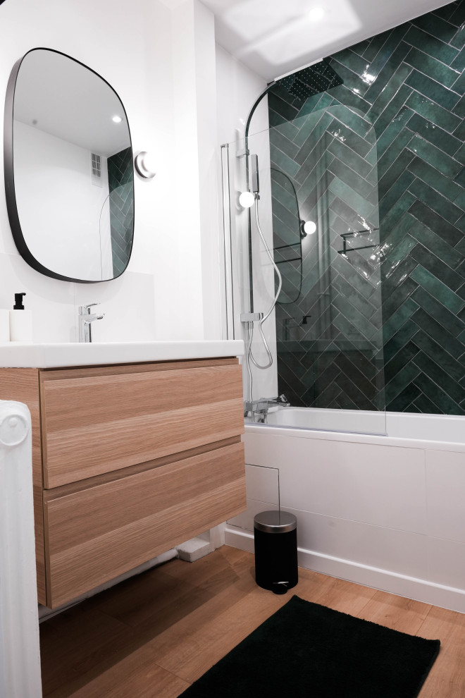 This is an example of a mid-sized contemporary master bathroom in Paris with an undermount tub, a single vanity, a floating vanity, shaker cabinets, light wood cabinets, a shower/bathtub combo, green tile, ceramic tile, white walls, light hardwood floors, a trough sink, beige floor and a hinged shower door.