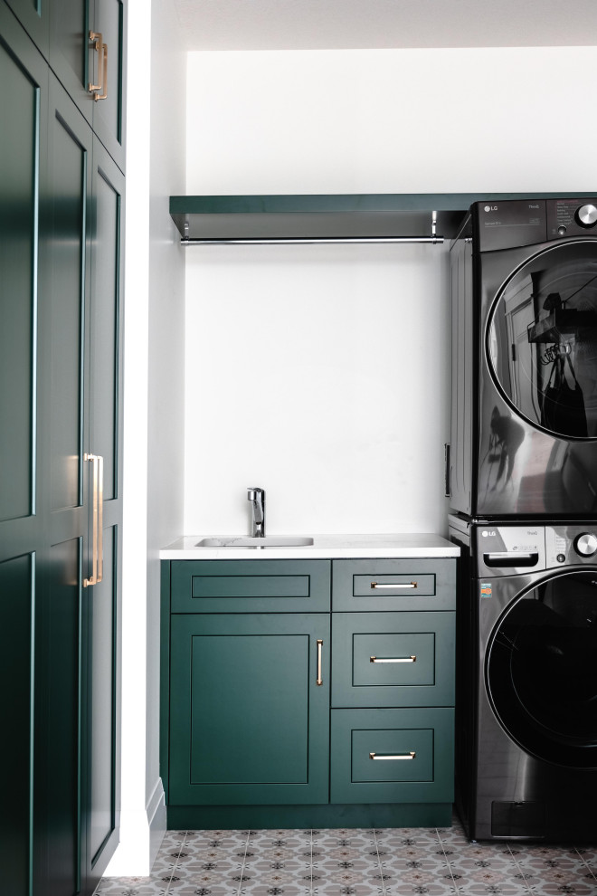 Inspiration for a large modern l-shaped dedicated laundry room in Toronto with an undermount sink, green cabinets, quartz benchtops, white walls, a stacked washer and dryer and white benchtop.