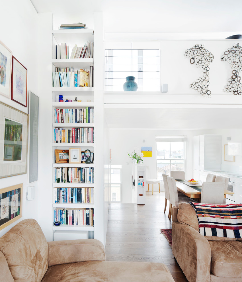 This is an example of a contemporary living room in London with a library, white walls and medium hardwood floors.
