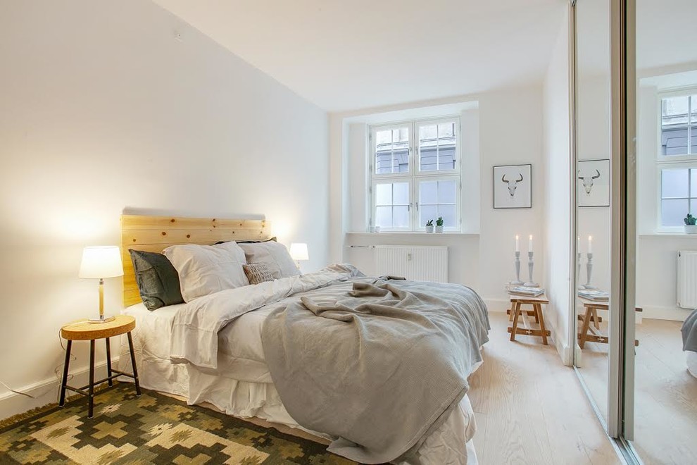 Scandinavian bedroom in Copenhagen with white walls, light hardwood floors and no fireplace.