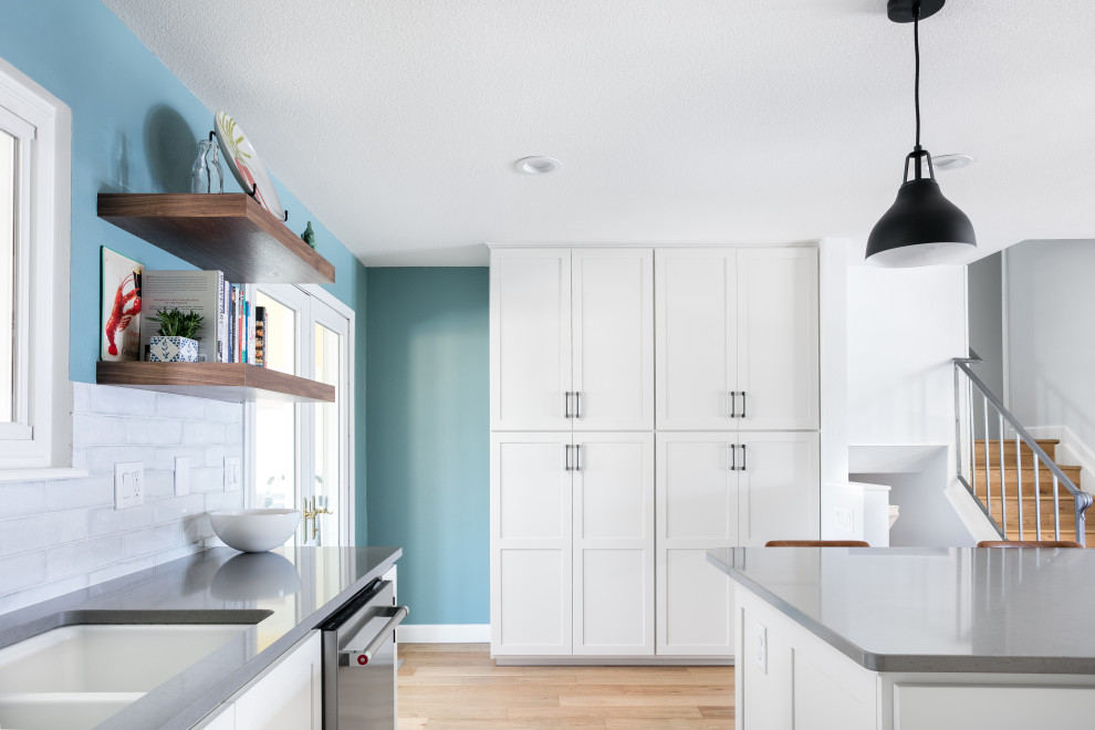 Example of a mid-sized transitional l-shaped light wood floor and brown floor eat-in kitchen design in Denver with an undermount sink, shaker cabinets, white cabinets, quartz countertops, white backsplash, porcelain backsplash, stainless steel appliances, an island and gray countertops
