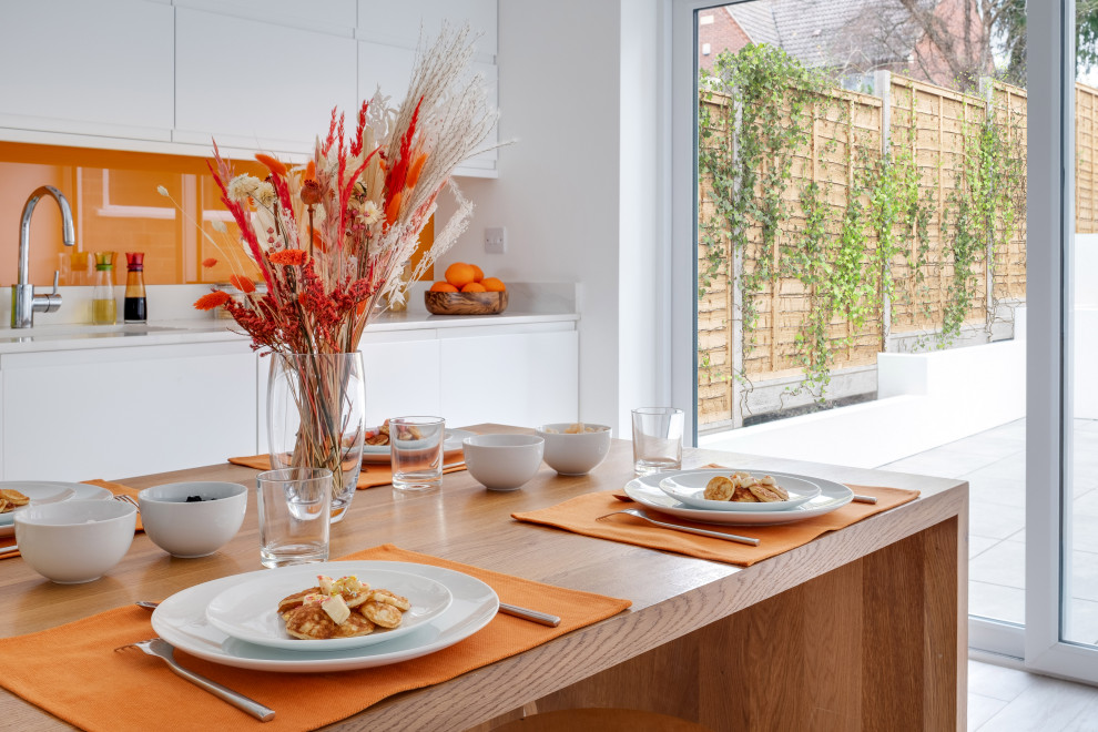 Immagine di una cucina minimal di medie dimensioni con lavello integrato, ante bianche, top in quarzo composito, paraspruzzi arancione, paraspruzzi con lastra di vetro, elettrodomestici da incasso, pavimento in gres porcellanato, pavimento beige e top bianco