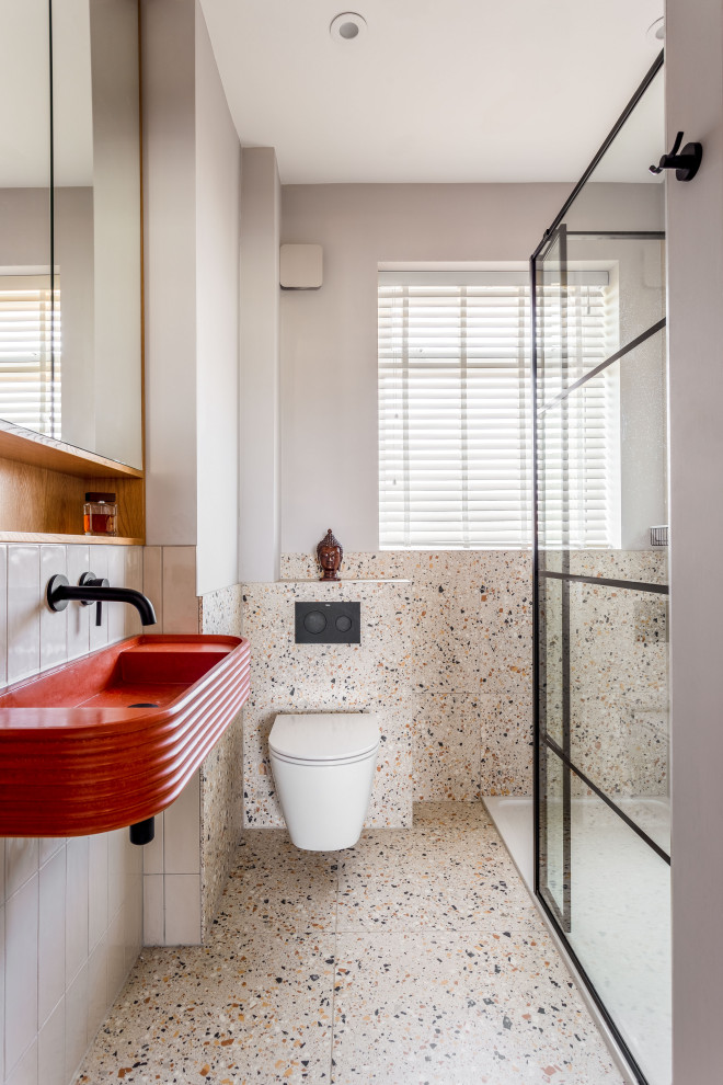 Exempel på ett litet eklektiskt orange oranget badrum med dusch, med luckor med profilerade fronter, orange skåp, en öppen dusch, en vägghängd toalettstol, grå kakel, keramikplattor, grå väggar, terrazzogolv, ett väggmonterat handfat, bänkskiva i betong, orange golv och dusch med gångjärnsdörr