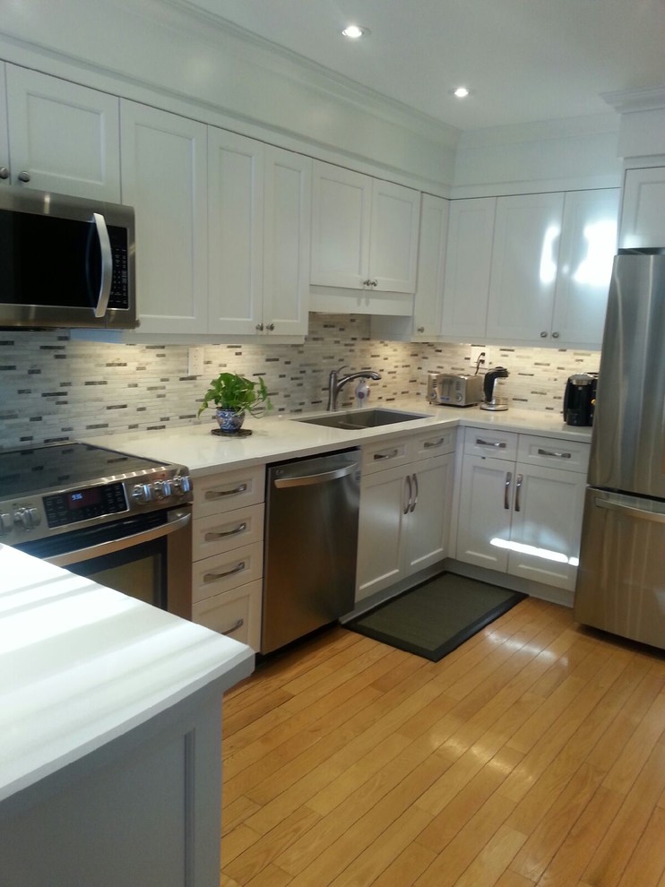 Open concept kitchen - mid-sized transitional u-shaped light wood floor open concept kitchen idea in Toronto with an undermount sink, shaker cabinets, white cabinets, quartz countertops, white backsplash, stone tile backsplash, stainless steel appliances and a peninsula