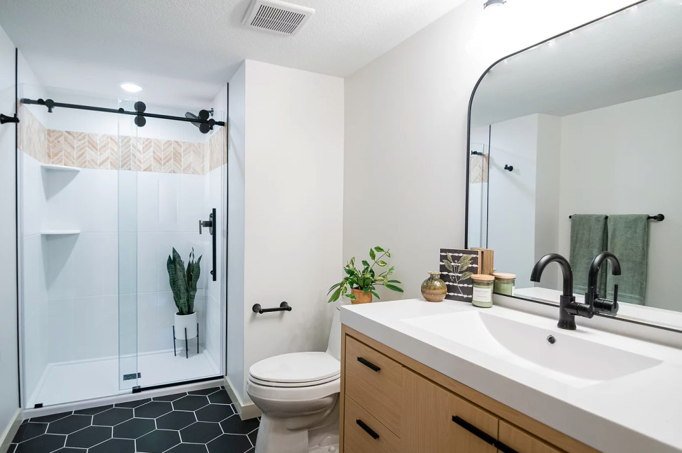 Photo of a mid-sized scandinavian 3/4 bathroom in Minneapolis with flat-panel cabinets, light wood cabinets, an alcove shower, white tile, ceramic tile, white walls, ceramic floors, an integrated sink, solid surface benchtops, black floor, a sliding shower screen, white benchtops, a single vanity and a freestanding vanity.