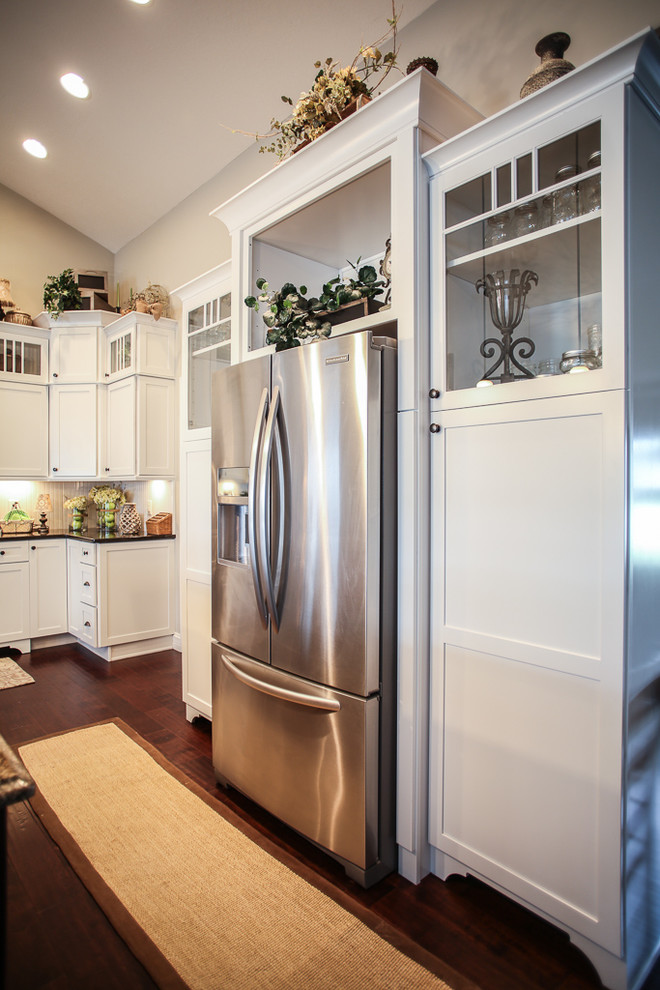 Transitional l-shaped dark wood floor open concept kitchen photo with a farmhouse sink, shaker cabinets, white cabinets, quartz countertops, white backsplash, stainless steel appliances and an island
