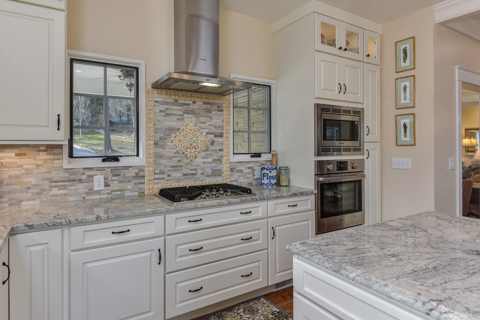 Large transitional l-shaped medium tone wood floor kitchen photo with a farmhouse sink, raised-panel cabinets, white cabinets, granite countertops, multicolored backsplash, matchstick tile backsplash, stainless steel appliances and an island