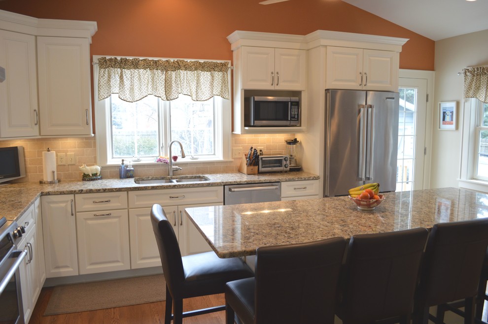 Enclosed kitchen - large transitional l-shaped medium tone wood floor enclosed kitchen idea in Columbus with an undermount sink, raised-panel cabinets, white cabinets, granite countertops, beige backsplash, stone tile backsplash, stainless steel appliances and an island