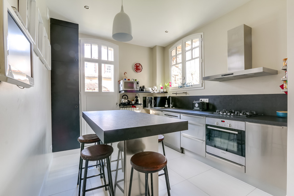 This is an example of a mid-sized traditional single-wall eat-in kitchen in Paris with black cabinets, black splashback, with island, black benchtop, beaded inset cabinets, granite benchtops, white floor, a single-bowl sink, cement tile splashback, stainless steel appliances and cement tiles.