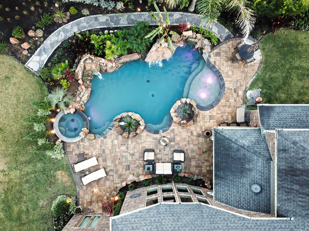 Inspiration for a large traditional backyard custom-shaped pool in Houston with a hot tub and natural stone pavers.
