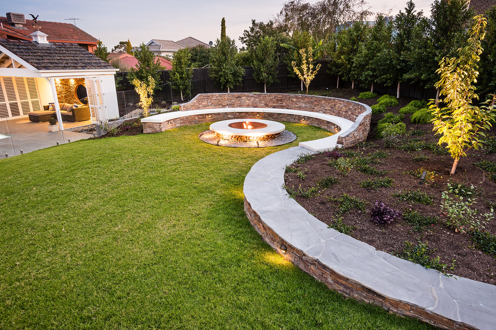 Expansive contemporary backyard full sun garden in Melbourne with a fire feature and natural stone pavers for spring.