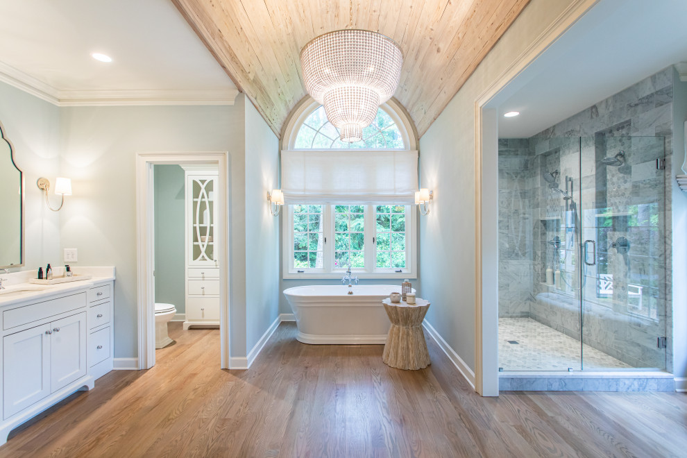 This is an example of a large transitional master bathroom in Atlanta with shaker cabinets, white cabinets, a freestanding tub, a double shower, a one-piece toilet, gray tile, medium hardwood floors, an undermount sink, a hinged shower door, white benchtops, a double vanity, a built-in vanity and wood.