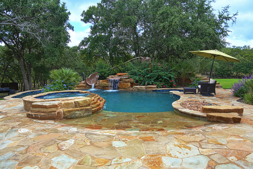 Large country backyard custom-shaped natural pool in Austin with natural stone pavers and a hot tub.