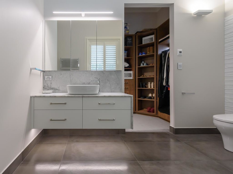 Photo of a mid-sized contemporary bathroom in Melbourne with flat-panel cabinets, white cabinets, an open shower, a two-piece toilet, white tile, ceramic tile, white walls, porcelain floors, a vessel sink, marble benchtops, grey floor and an open shower.