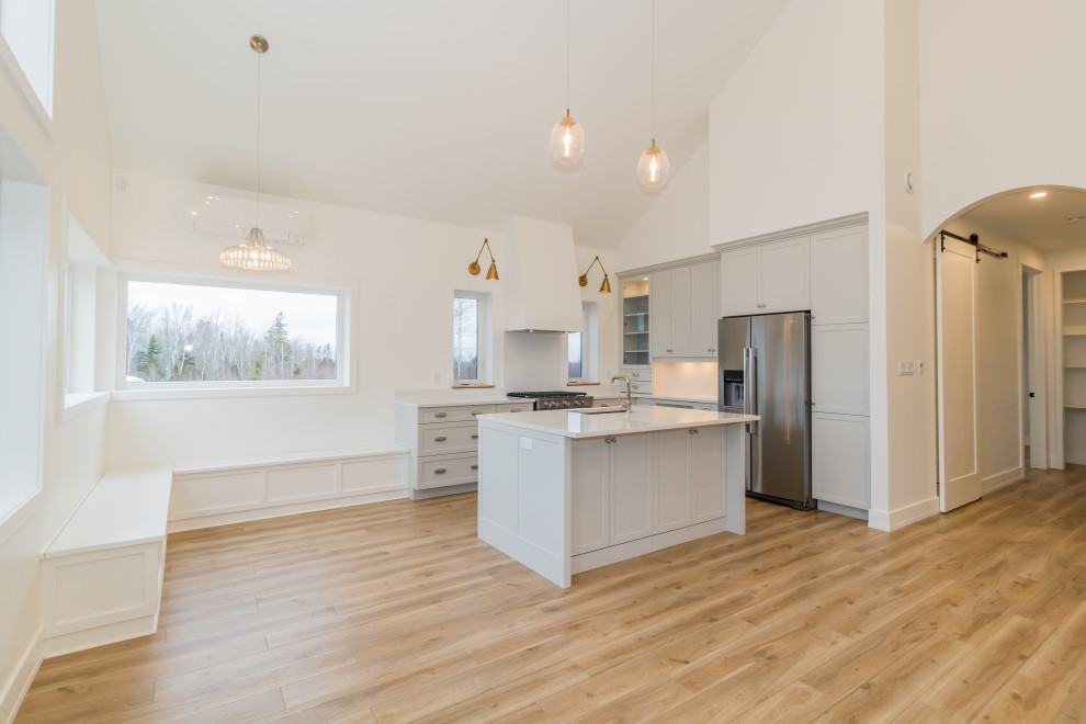 Mid-sized l-shaped light wood floor and brown floor kitchen photo with recessed-panel cabinets, blue cabinets, quartzite countertops, stainless steel appliances, an island and white countertops