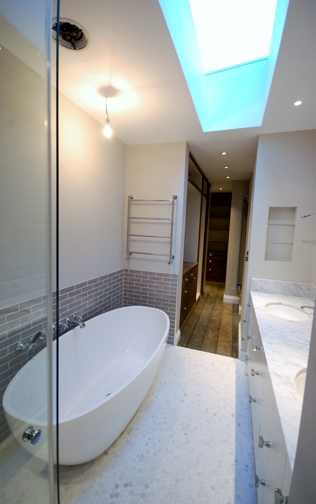 This is an example of a mid-sized contemporary master bathroom in London with an undermount sink, flat-panel cabinets, white cabinets, marble benchtops, a drop-in tub, an open shower, a wall-mount toilet, gray tile, ceramic tile, grey walls and mosaic tile floors.