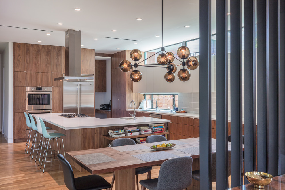 Photo of a mid-sized contemporary l-shaped eat-in kitchen in Houston with light hardwood floors, brown floor, an undermount sink, flat-panel cabinets, medium wood cabinets, grey splashback, stainless steel appliances and with island.