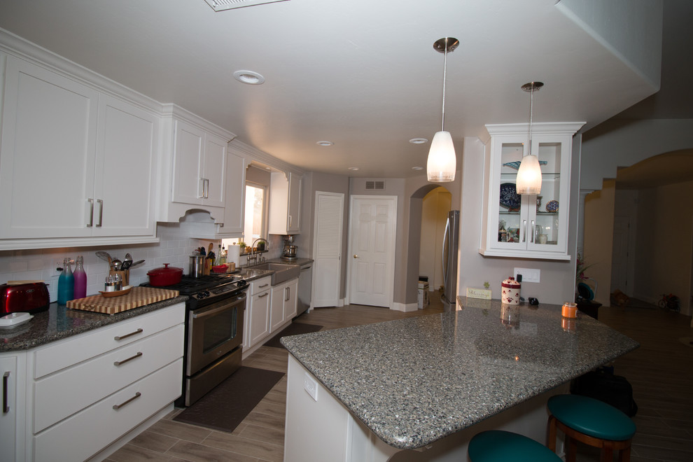 Example of a mid-sized transitional galley porcelain tile open concept kitchen design with a farmhouse sink, shaker cabinets, white cabinets, quartz countertops, white backsplash, subway tile backsplash and stainless steel appliances