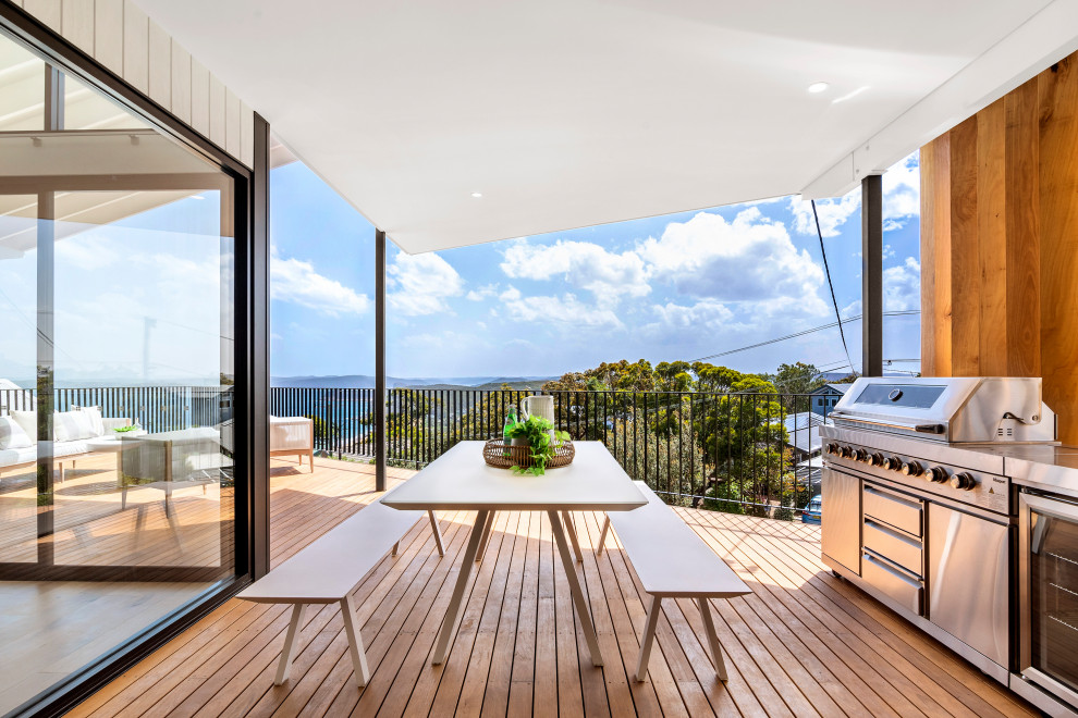 This is an example of a large beach style deck in Sydney with an outdoor kitchen and a roof extension.