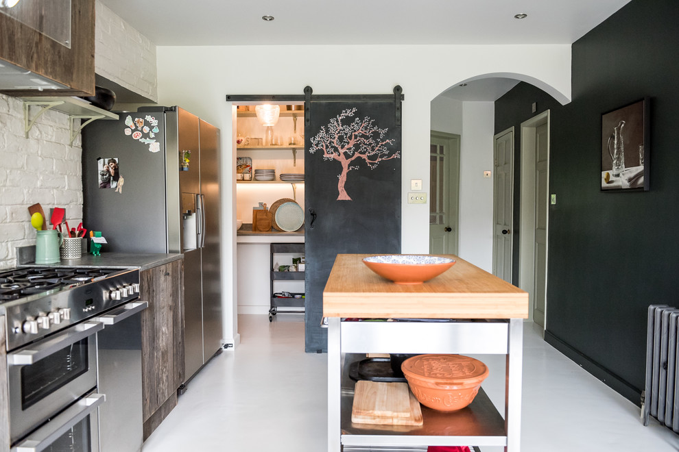 This is an example of a mid-sized eclectic single-wall open plan kitchen in London with a single-bowl sink, flat-panel cabinets, medium wood cabinets, concrete benchtops, white splashback, brick splashback, stainless steel appliances, with island, white floor and grey benchtop.