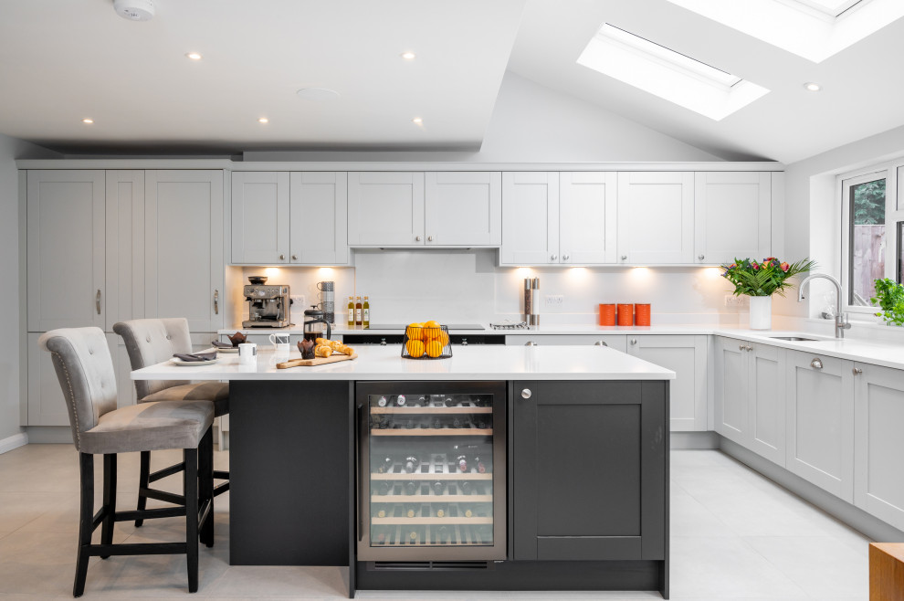 Photo of a large transitional l-shaped open plan kitchen in Surrey with a drop-in sink, shaker cabinets, grey cabinets, quartzite benchtops, white splashback, engineered quartz splashback, panelled appliances, porcelain floors, with island, grey floor and white benchtop.