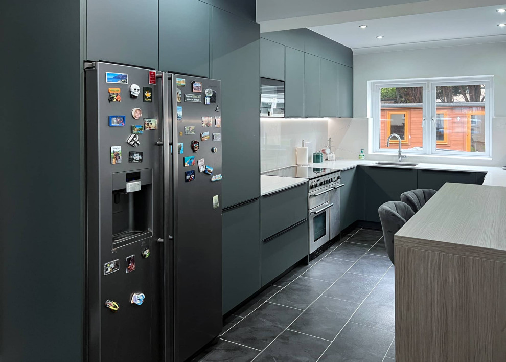 This is an example of a small contemporary enclosed kitchen in London with flat-panel cabinets, green cabinets, stainless steel appliances, grey floors and white worktops.