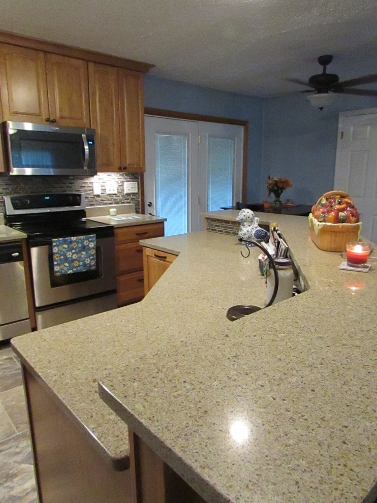 Example of a mid-sized transitional l-shaped ceramic tile home design design with a double-bowl sink, raised-panel cabinets, light wood cabinets, quartz countertops, multicolored backsplash, mosaic tile backsplash, stainless steel appliances and an island
