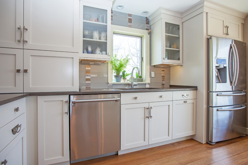 Example of a large transitional l-shaped medium tone wood floor eat-in kitchen design in Boston with an undermount sink, shaker cabinets, white cabinets, quartz countertops, gray backsplash, glass sheet backsplash, stainless steel appliances and an island