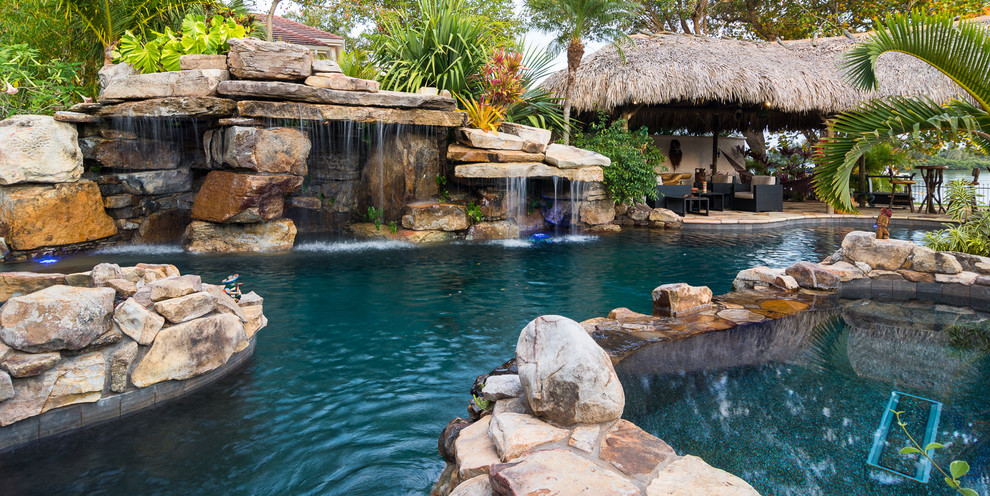 Expansive tropical backyard custom-shaped natural pool in Tampa with a hot tub and natural stone pavers.