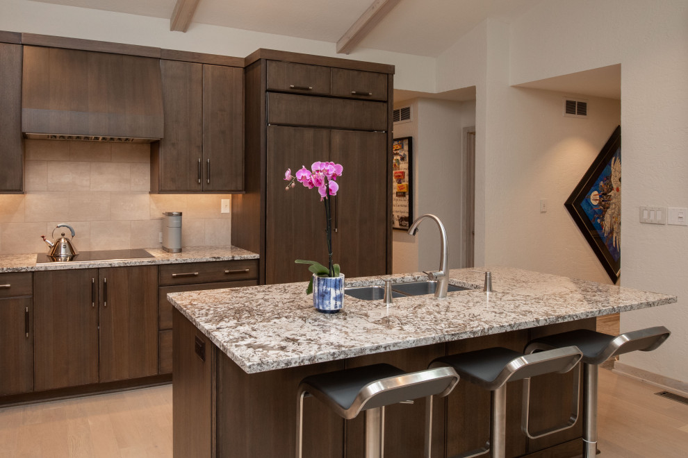 Mid-sized contemporary l-shaped open plan kitchen in Indianapolis with an undermount sink, flat-panel cabinets, dark wood cabinets, granite benchtops, beige splashback, porcelain splashback, panelled appliances, light hardwood floors, with island, brown floor, brown benchtop and vaulted.