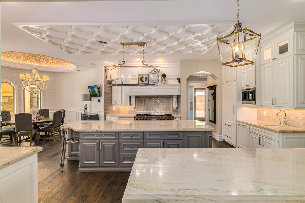 Large transitional u-shaped eat-in kitchen in Phoenix with an undermount sink, beaded inset cabinets, white cabinets, marble benchtops, grey splashback, ceramic splashback, panelled appliances, medium hardwood floors, with island, brown floor and multi-coloured benchtop.
