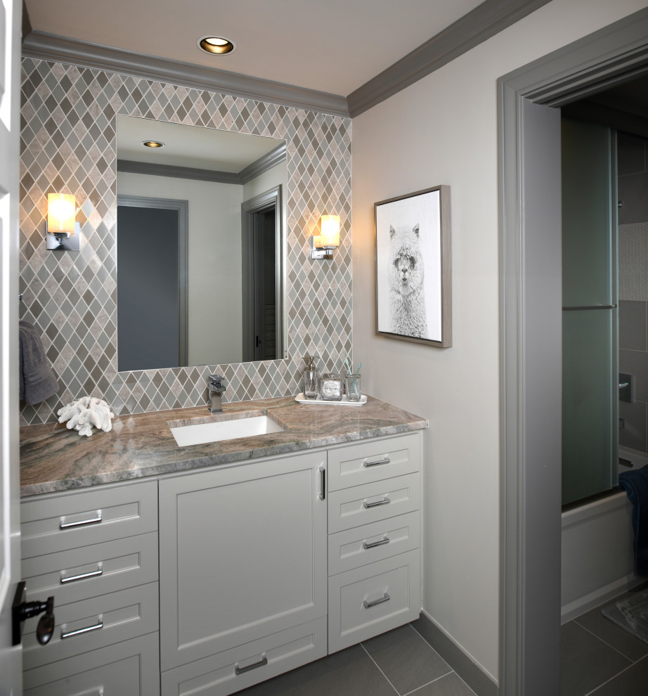 This is an example of a mid-sized transitional kids bathroom in Houston with shaker cabinets, grey cabinets, an alcove tub, a shower/bathtub combo, a one-piece toilet, multi-coloured tile, glass sheet wall, grey walls, porcelain floors, an undermount sink, quartzite benchtops, grey floor, a sliding shower screen and multi-coloured benchtops.