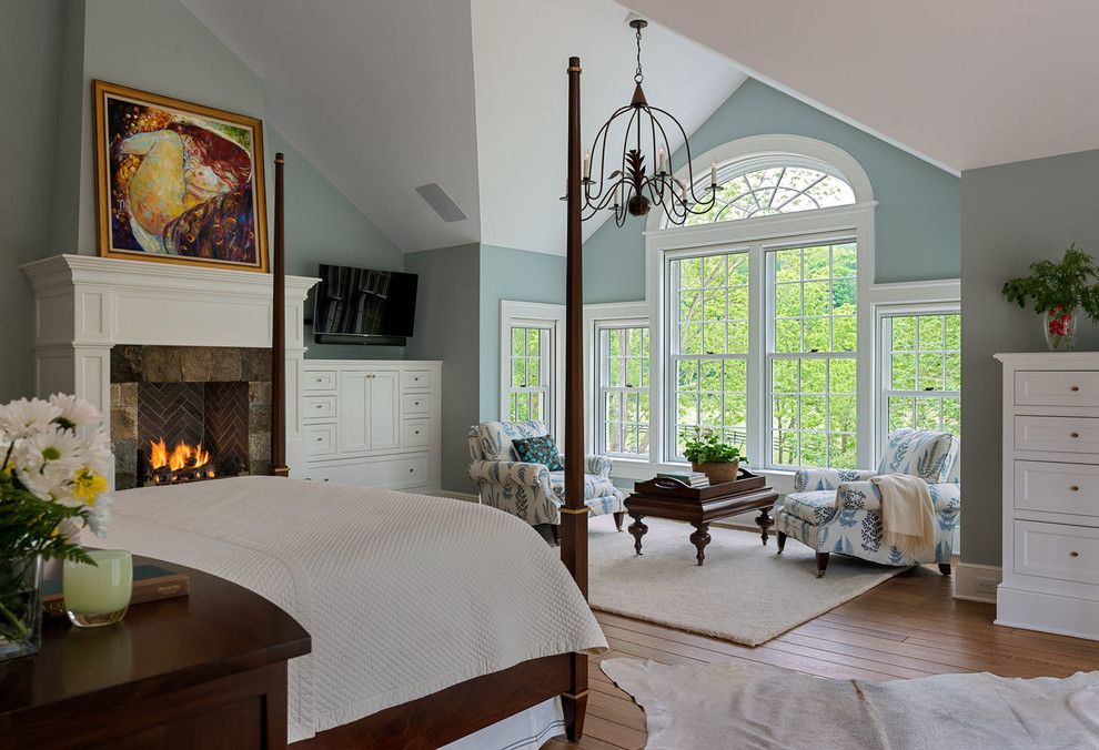 This is an example of a large traditional master bedroom in New York with blue walls, a standard fireplace, light hardwood floors and a stone fireplace surround.