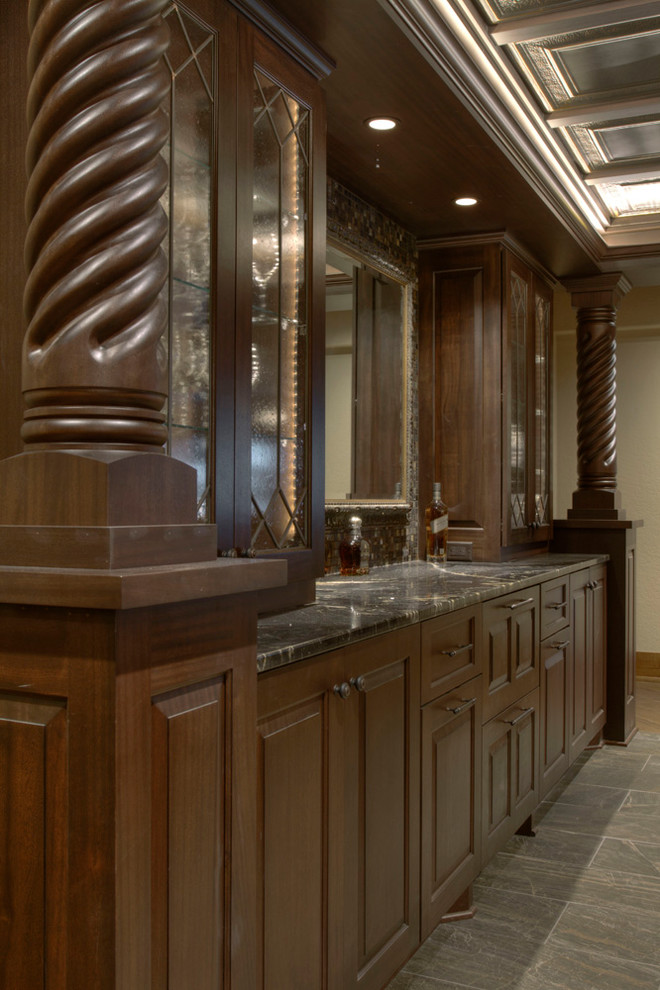 Photo of an expansive traditional u-shaped seated home bar in Minneapolis with a drop-in sink, raised-panel cabinets, dark wood cabinets, granite benchtops, brown splashback and porcelain floors.