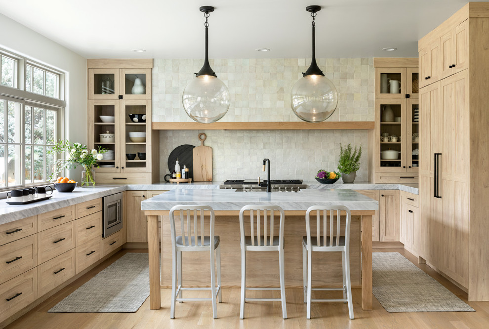 Inspiration for a medium sized farmhouse u-shaped kitchen in Denver with glass-front cabinets, light wood cabinets, grey splashback, stone tiled splashback, stainless steel appliances, light hardwood flooring, an island and brown floors.