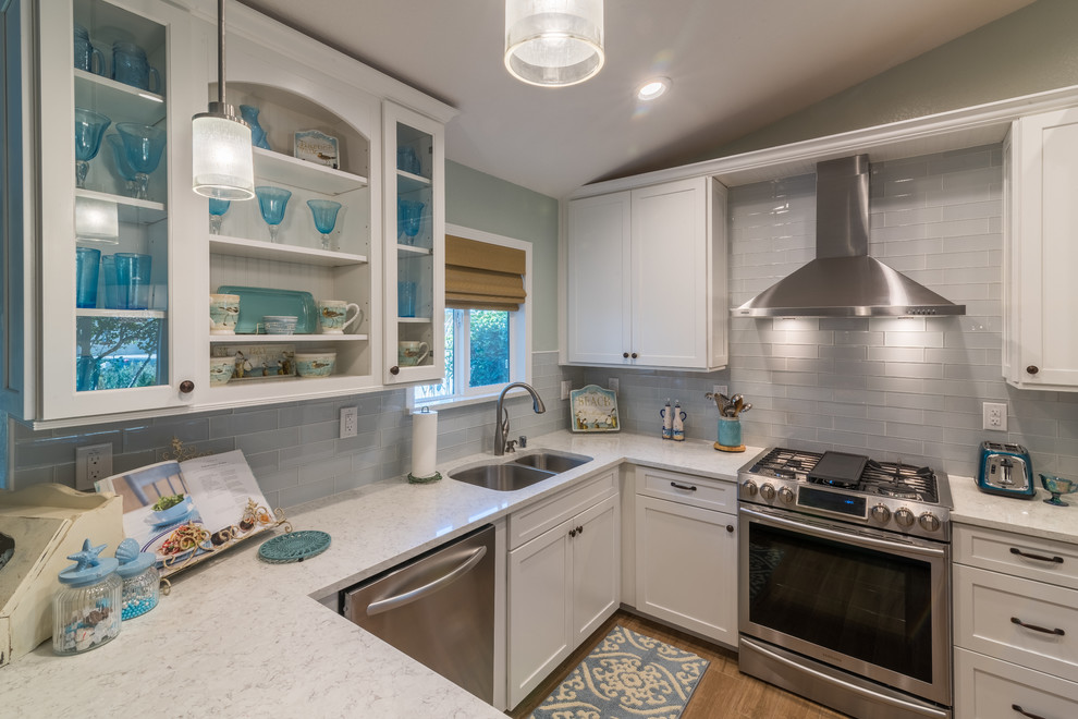 Inspiration for a mid-sized beach style u-shaped eat-in kitchen in Sacramento with an undermount sink, glass-front cabinets, white cabinets, marble benchtops, white splashback, glass tile splashback, stainless steel appliances, ceramic floors and a peninsula.