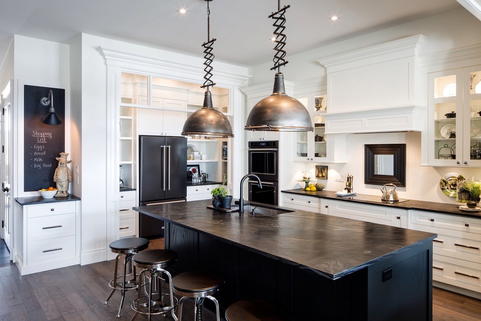 Large trendy galley medium tone wood floor and brown floor open concept kitchen photo with an undermount sink, shaker cabinets, white cabinets, granite countertops, white backsplash, stainless steel appliances and an island
