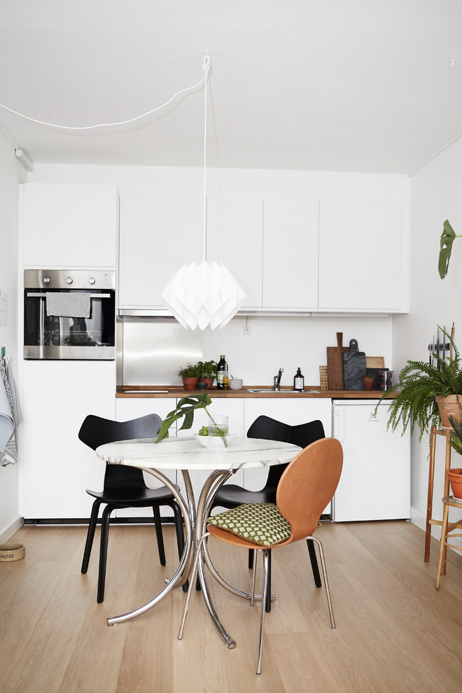 Design ideas for a small scandinavian eat-in kitchen in Wiltshire with flat-panel cabinets, white cabinets, wood benchtops, light hardwood floors, no island and brown benchtop.